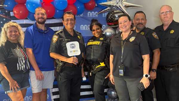 Group photo of community members, sheriff’s deputies, and volunteers posing in front of a National Night Out backdrop decorated with red, white, blue, and silver balloons.